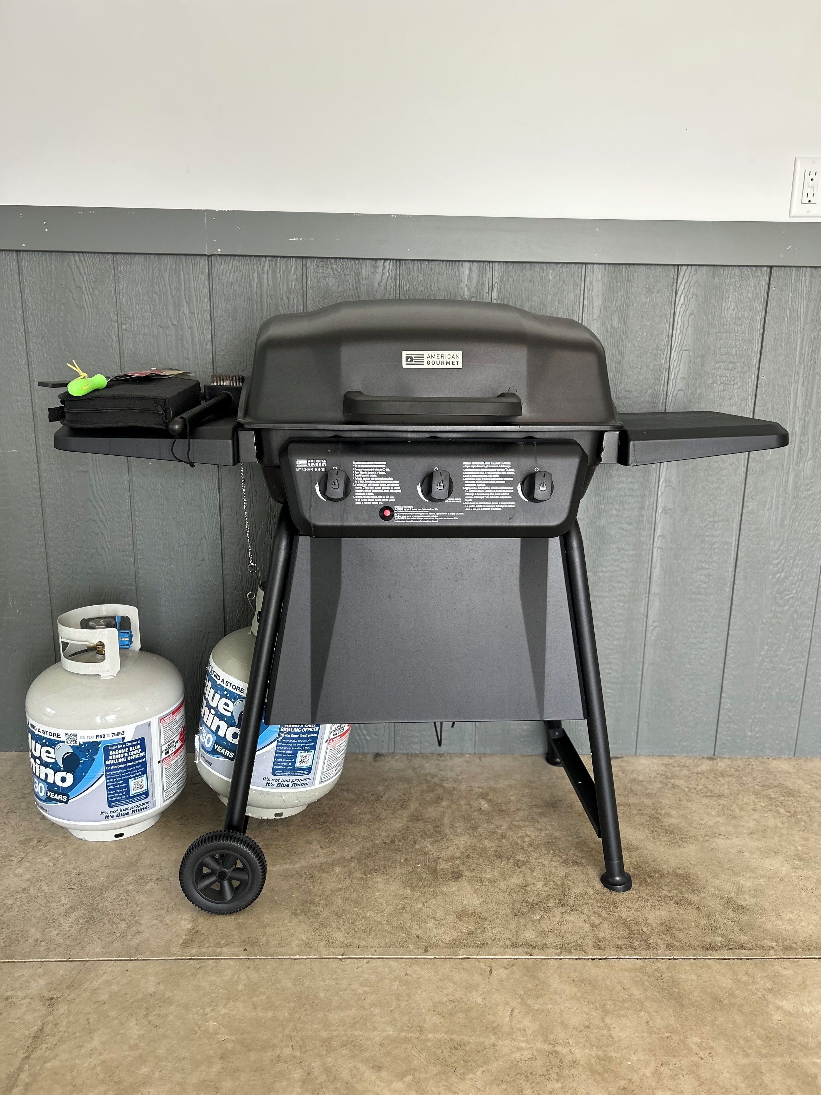 A portable grill with a control panel, a side shelf, and a gas tank nearby.