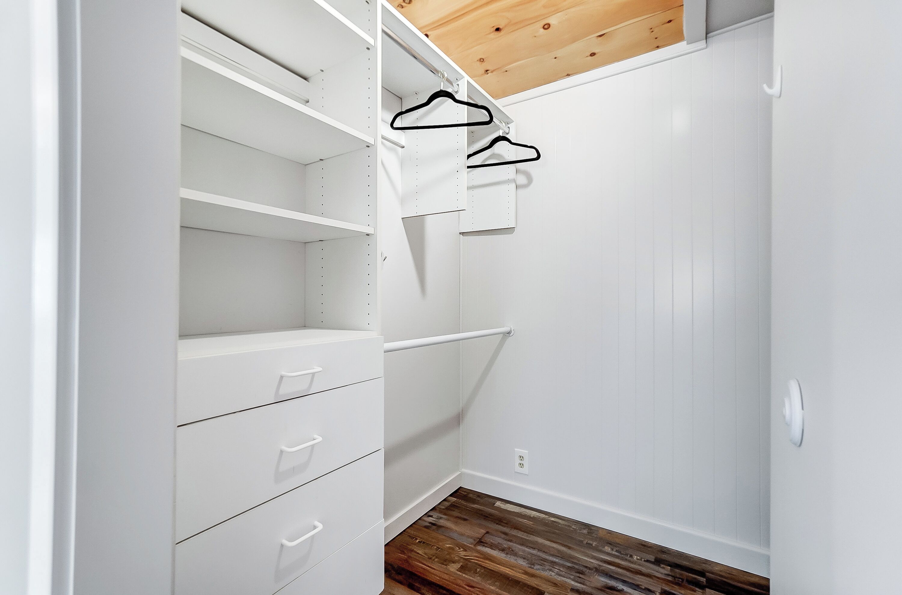 Un placard blanc avec des étagères ouvertes, un plafond en bois et un plancher en bois.