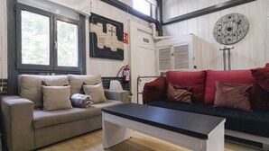 Ein modernes Wohnzimmer mit einem grauen Sofa, einem roten Sofa und einem schwarzen Couchtisch. Ein Feuerlöscher und ein Kleiderständer sind zu sehen.