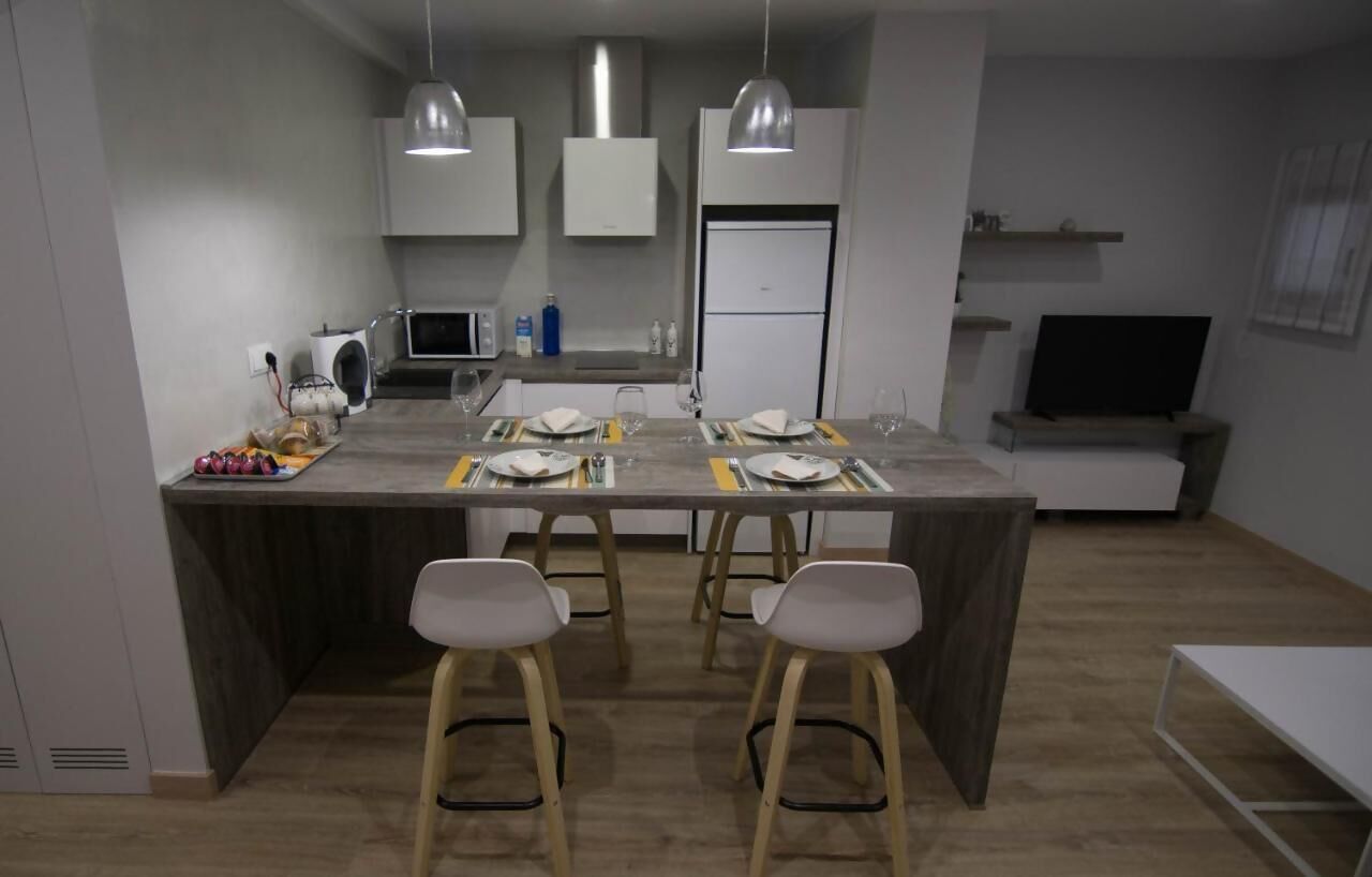 A modern kitchen with a central island, bar stools, and a dining table set for four.