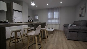 Une cuisine moderne avec des tabourets de bar blancs, une table à manger et un canapé gris.