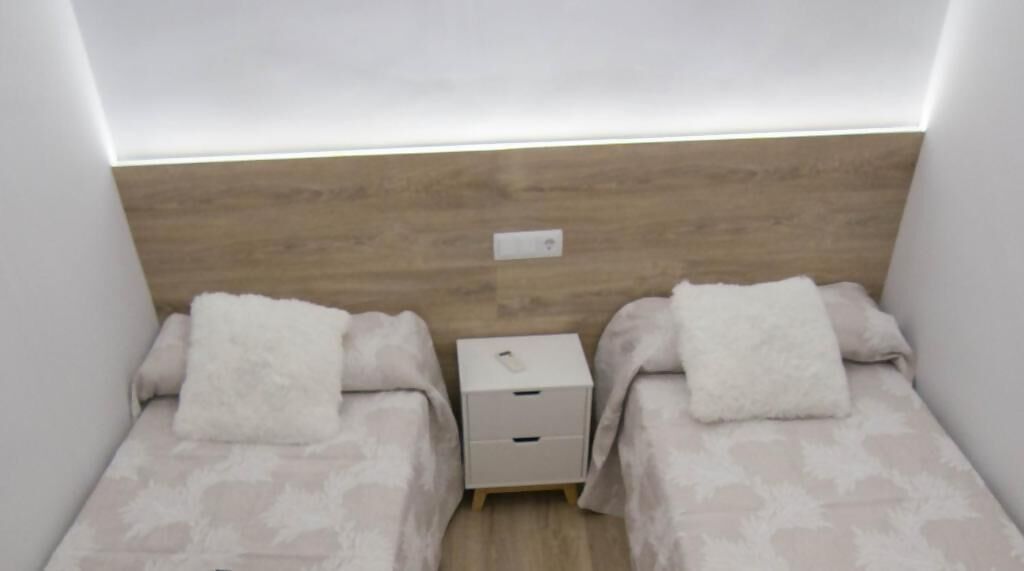 A small, modern bedroom with two beds, a nightstand, and a bedside table.