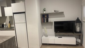 Une cuisine moderne avec des appareils électroménagers blancs, un téléviseur encastré et une petite étagère où sont posés des livres et des objets décoratifs.