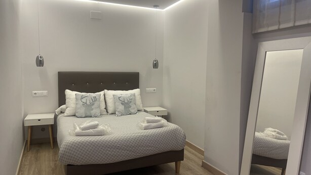 Une chambre bien rangée, avec un lit, des tables de chevet, un miroir et un luminaire au plafond.