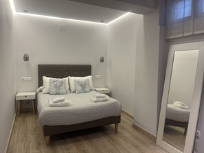 Un dormitorio ordenado con cama, mesitas de noche, un espejo y una lámpara en el techo.