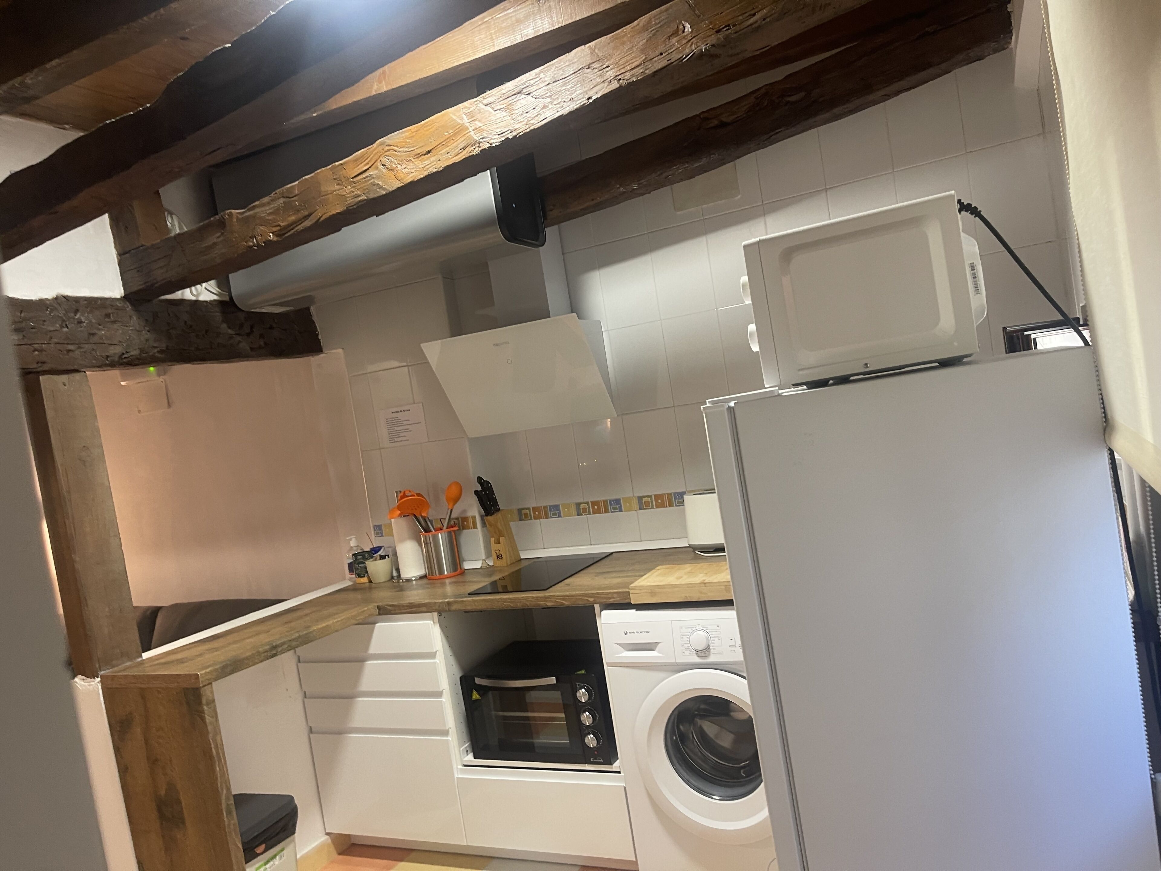 Eine kleine Küche mit Waschmaschine, Mikrowelle und Holzbalken.