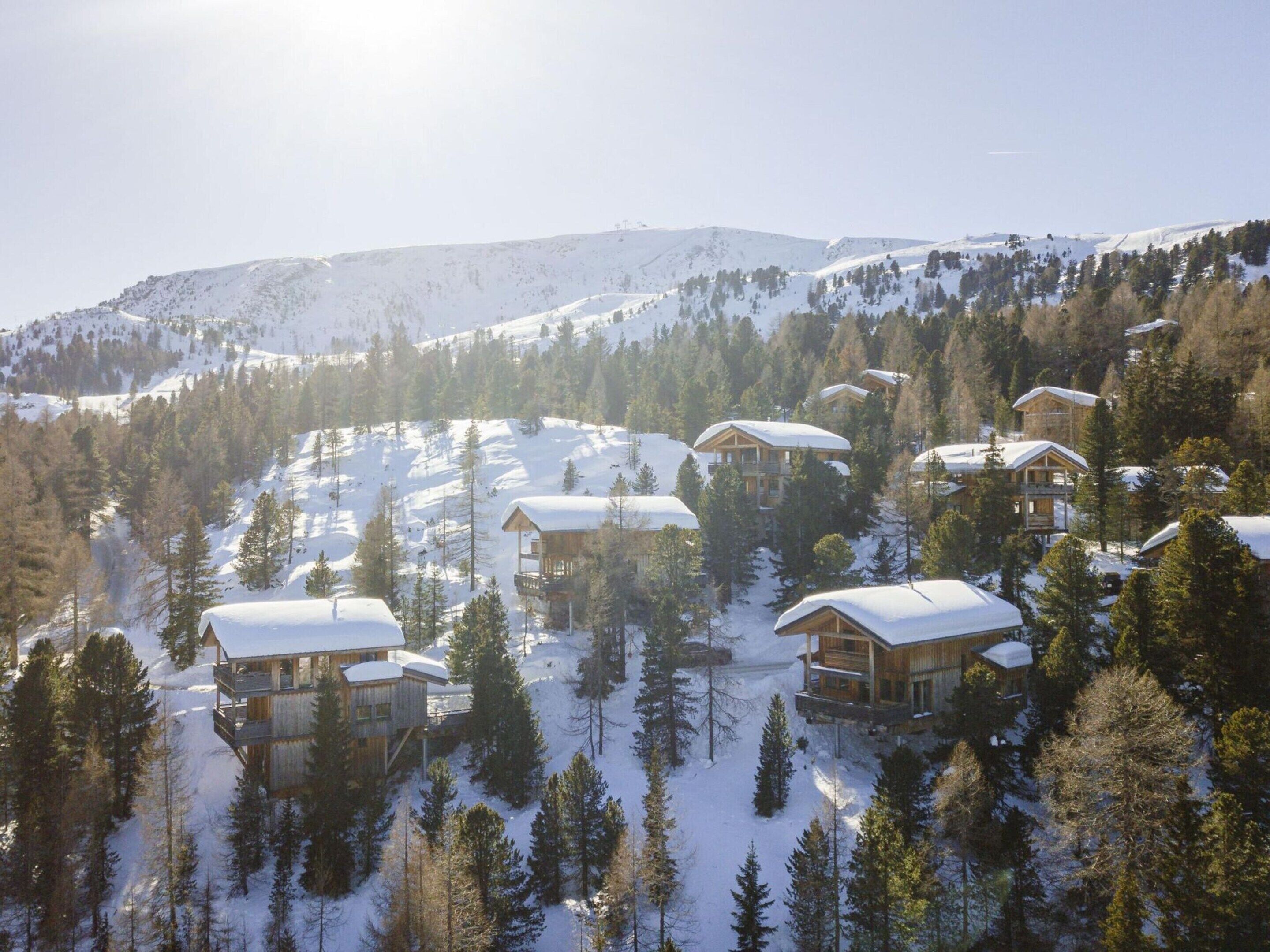 A cluster of wooden cabins on a snowy mountain slope, surrounded by trees.