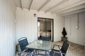 Relax in this cozy patio area with a glass table and four chairs, surrounded by a sloped ceiling and white paneled walls.