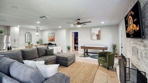 A modern living room with a grey sectional sofa, a green armchair, a pool table, and a fireplace. - Modern Tempe Retreat w/Hot Tub

 (Tempe)