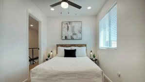 Une chambre à coucher avec un cadre de lit en bois, du linge de lit blanc, un ventilateur de plafond et une fenêtre avec des stores.