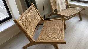 Two wicker chairs with a woven seat and backrest, positioned next to a window with a view of a parking lot.