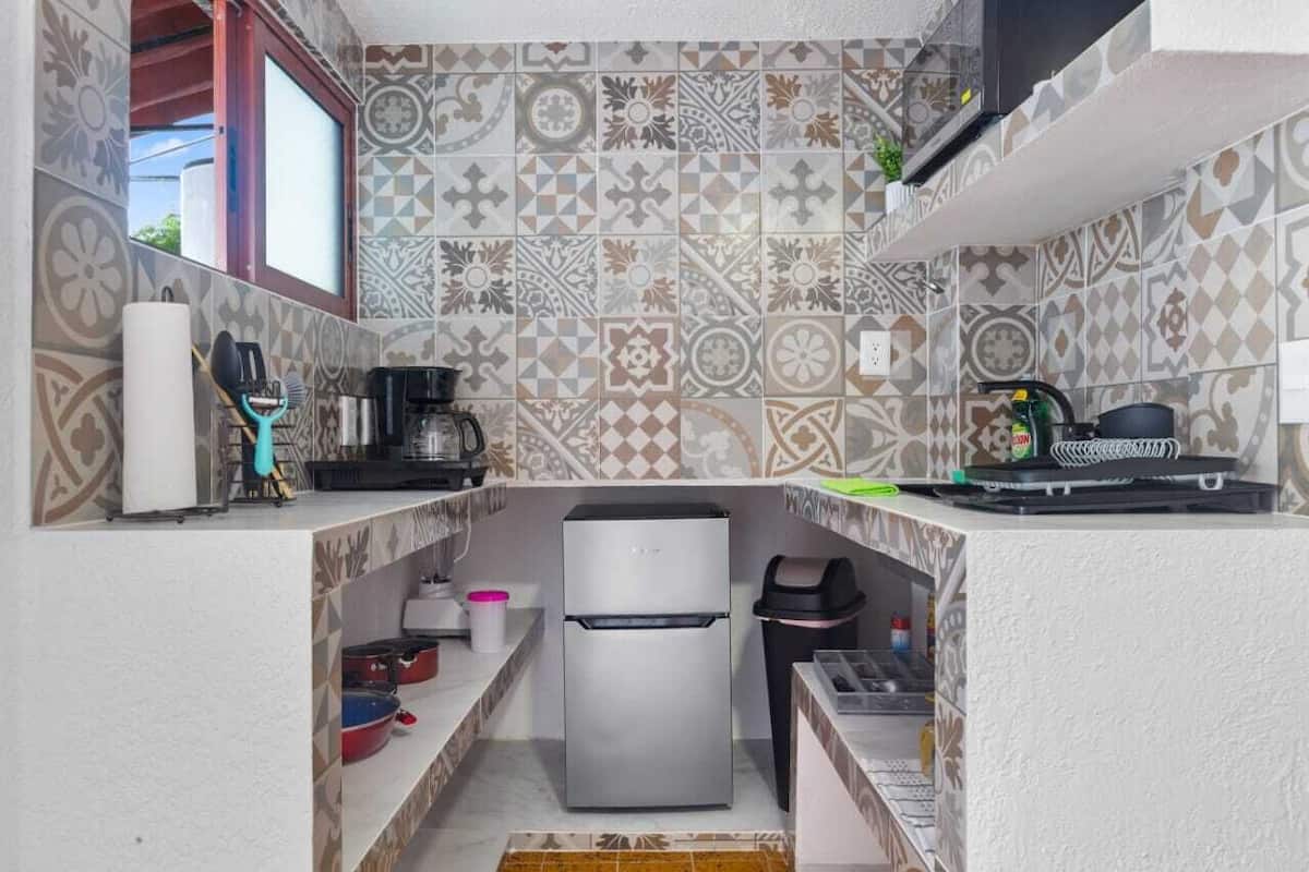 Una cocina compacta con baldosas estampadas, un refrigerador de acero inoxidable, una cafetera y un lavamanos pequeño.