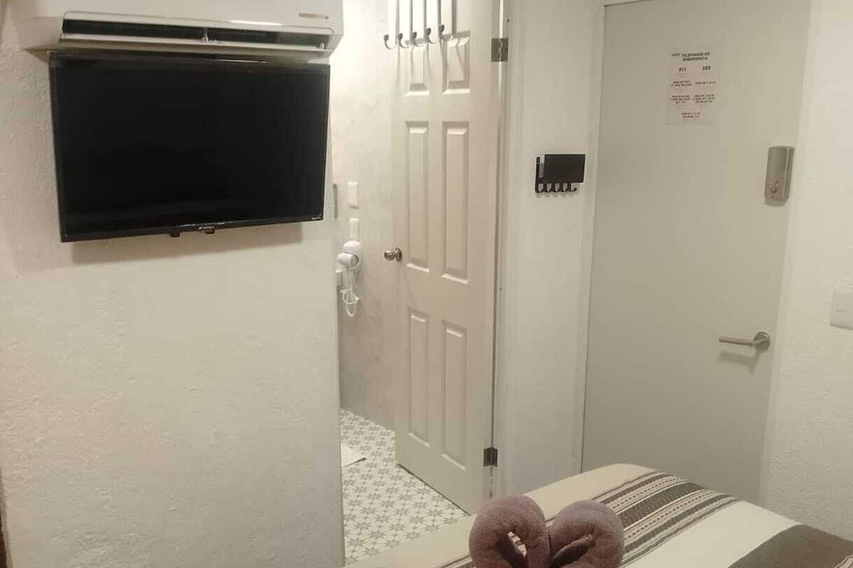 Habitación de hotel con cama, televisor de pantalla plana montado en la pared, puerta con un cartel y suelo de baldosas.