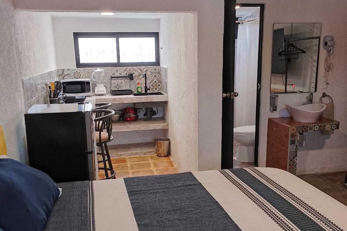 Un dormitorio compacto con cama, kitchenette pequeña y baño.