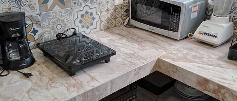 A kitchen with a microwave, coffee maker, and blender on a marble countertop.
