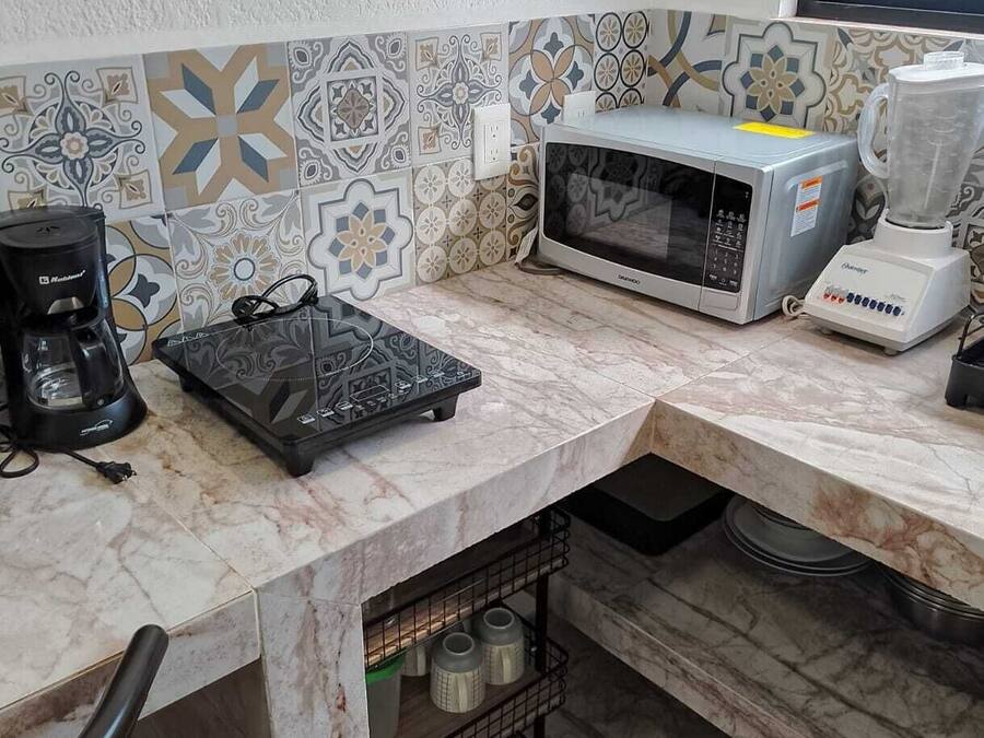 A kitchen with a microwave, coffee maker, and blender on a marble countertop.
