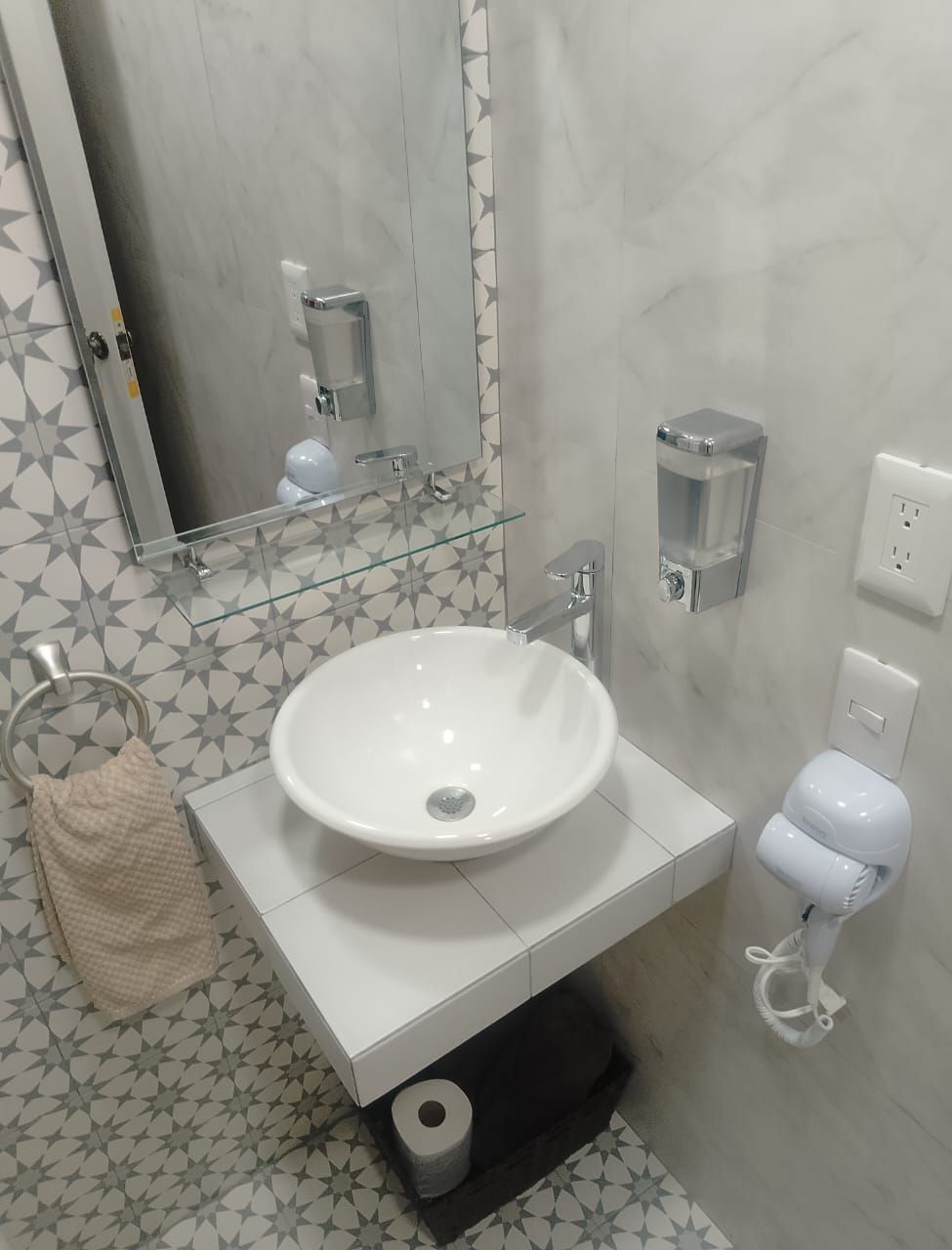 A bathroom with a white sink, a mirror, a towel rack, a toilet with a hand dryer, and a soap dispenser.