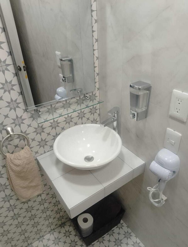 Un baño con un lavamanos blanco, un espejo, un perchero para toallas, un inodoro con secamanos y un dispensador de jabón.