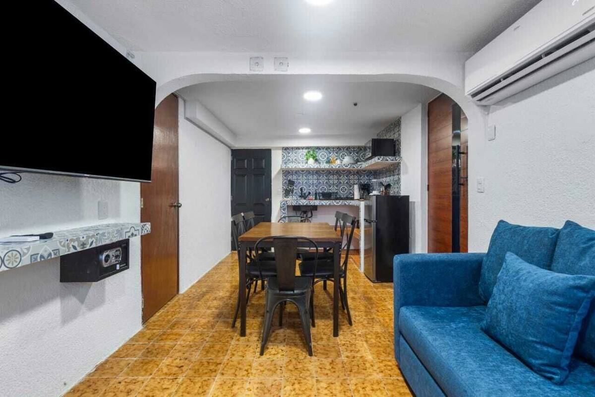 Un espacio habitable compacto con comedor, kitchenette y sofá azul.