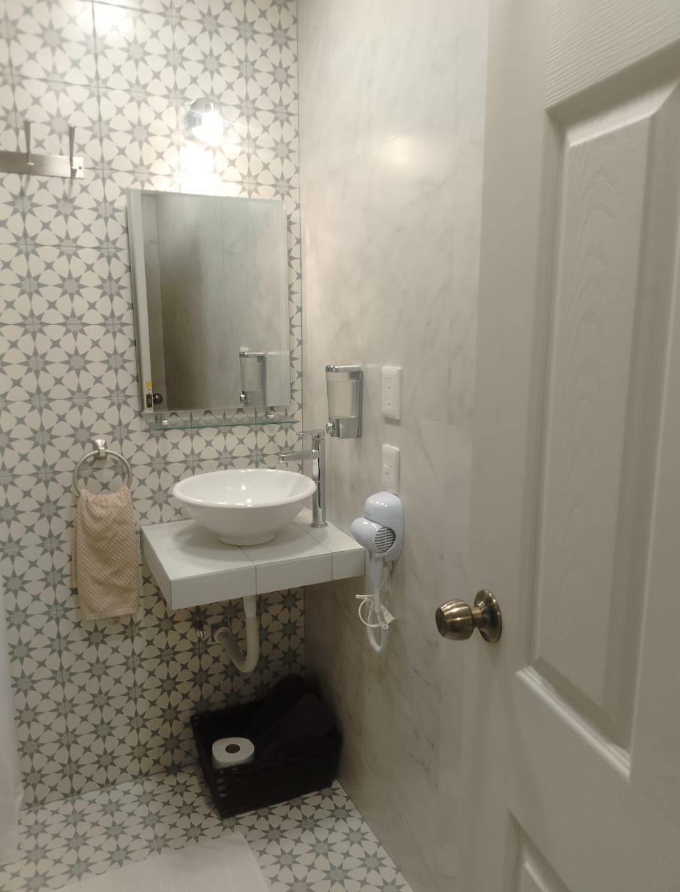 A bathroom with a white sink, mirror, and towel rack. There is a toilet paper holder and a hairdryer on the wall.