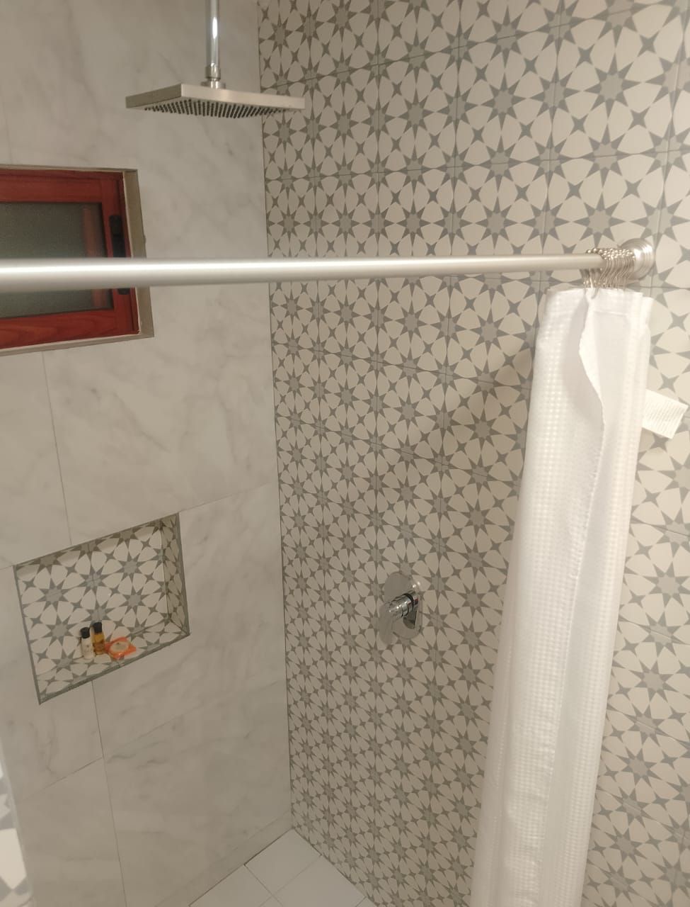 A shower area with a patterned tile wall, a metal showerhead, and a white shower curtain.