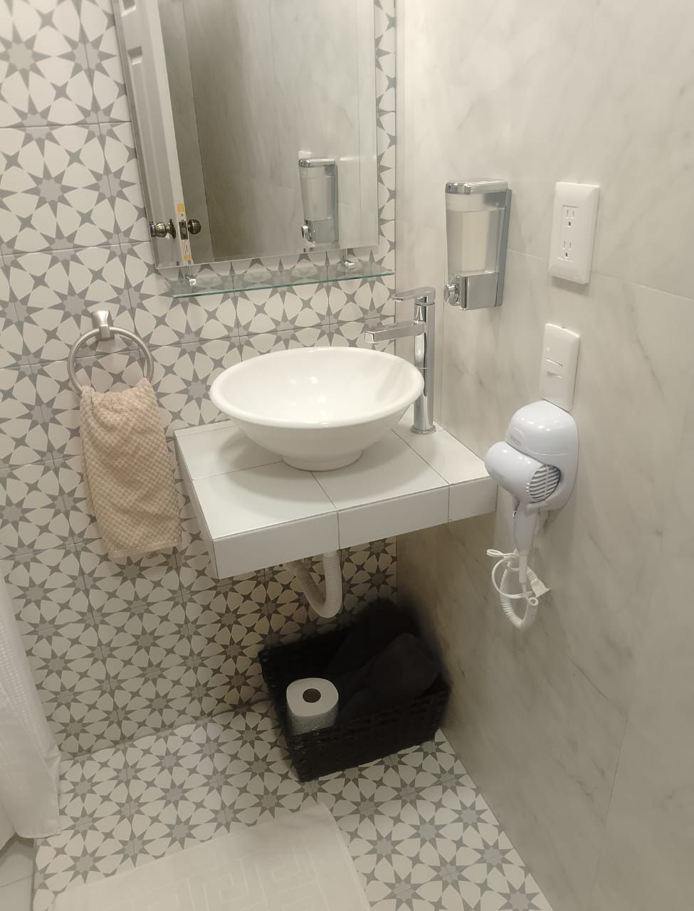 A bathroom with a white sink, a glass mirror, a towel ring, a toilet paper holder, and a hairdryer.