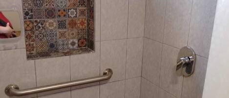 Une salle de bain équipée d’une barre d’appui, d’une douche et d’un revêtement mural décoratif en carreaux.