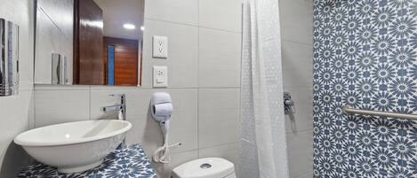 Un baño con un lavamanos blanco, un inodoro y una ducha con cortina estampada.