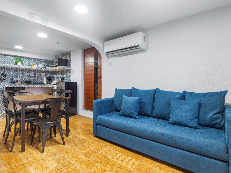 A compact living space with a dining area, a blue sofa, and a kitchen with patterned tiles.