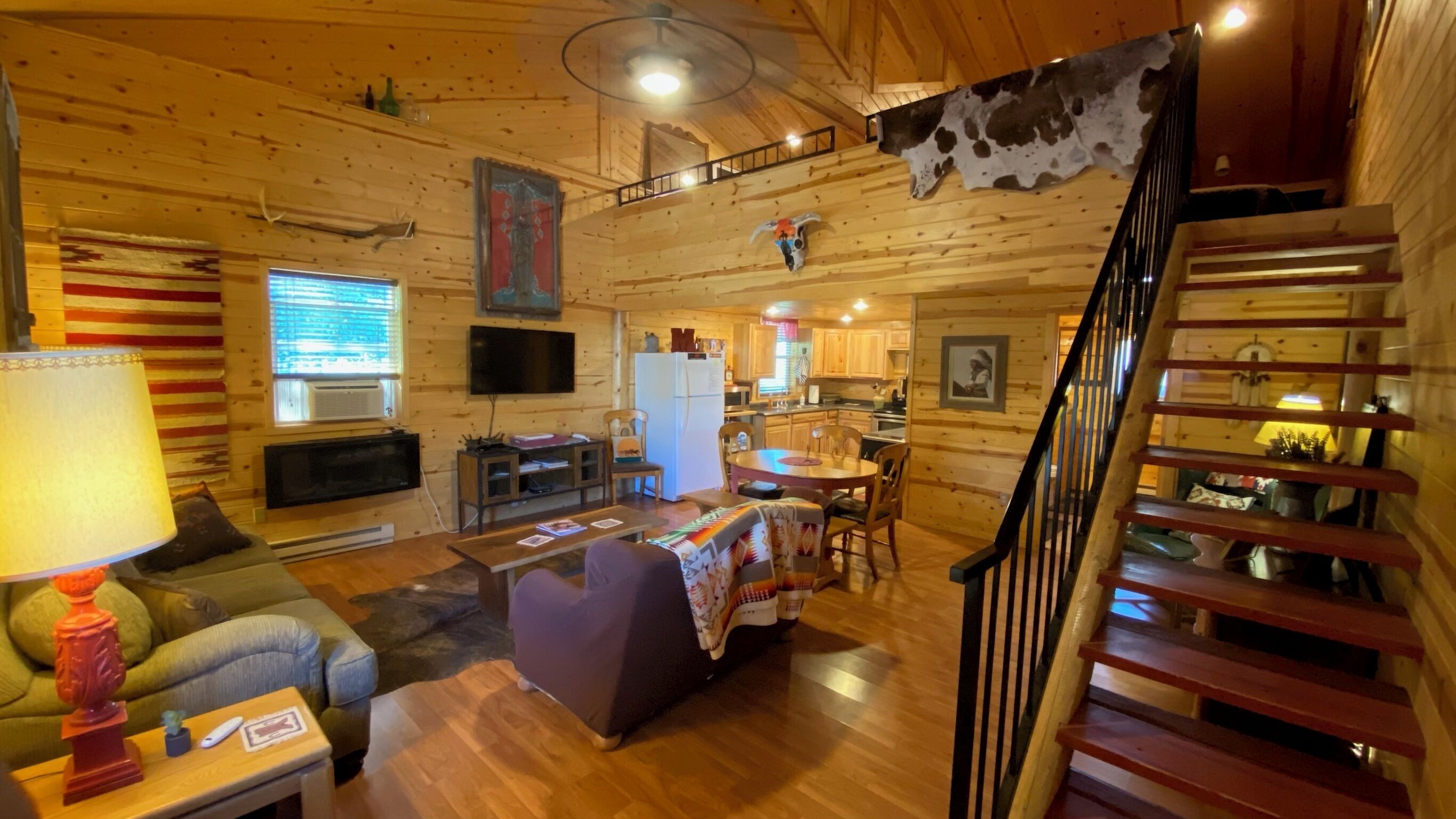 Un intérieur de chalet chaleureux comprenant un salon, un coin repas, une cuisine et un escalier en bois.