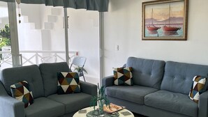 A living room with two grey sofas, a white coffee table, and a painting of boats on the wall. - Cozy 2-bedroom condo in awesome Sosúa with AC, WiFi, and a gorgeous pool
 (Sosúa)