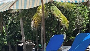 A beach with blue lounge chairs and striped umbrellas. - Cozy 2-bedroom condo in awesome Sosúa with AC, WiFi, and a gorgeous pool
 (Sosúa)