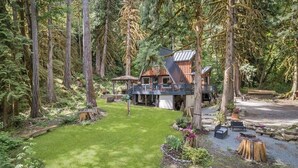 Een chalet omringd door hoge bomen, een terras en een verzorgd gazon.