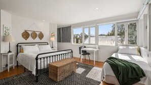 A bedroom with a bed, bedside tables, a chair, a small table, and a window with a view of the outside.