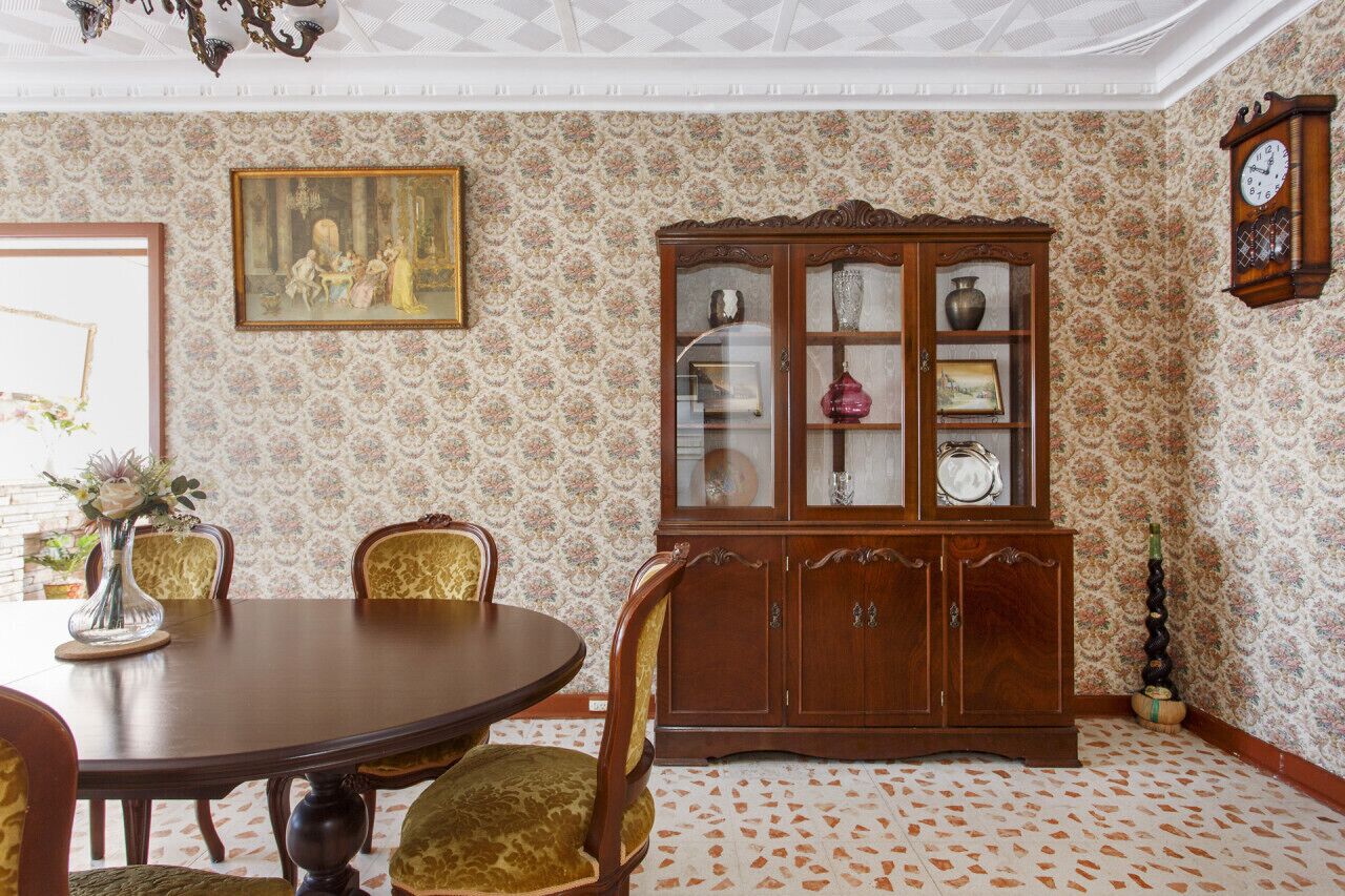 A dining room with a round table, chairs, a cabinet, and a clock on the wall.
