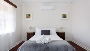 A hotel room with a bed, two bedside tables, an air conditioning unit, and two framed pictures on the wall. - Villa Fiore- South Fremantle Retro Style (Beaconsfield)