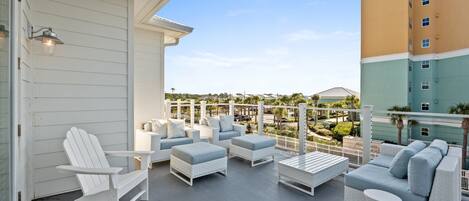 A balcony with white Adirondack chairs, a white sofa, and a small round table.