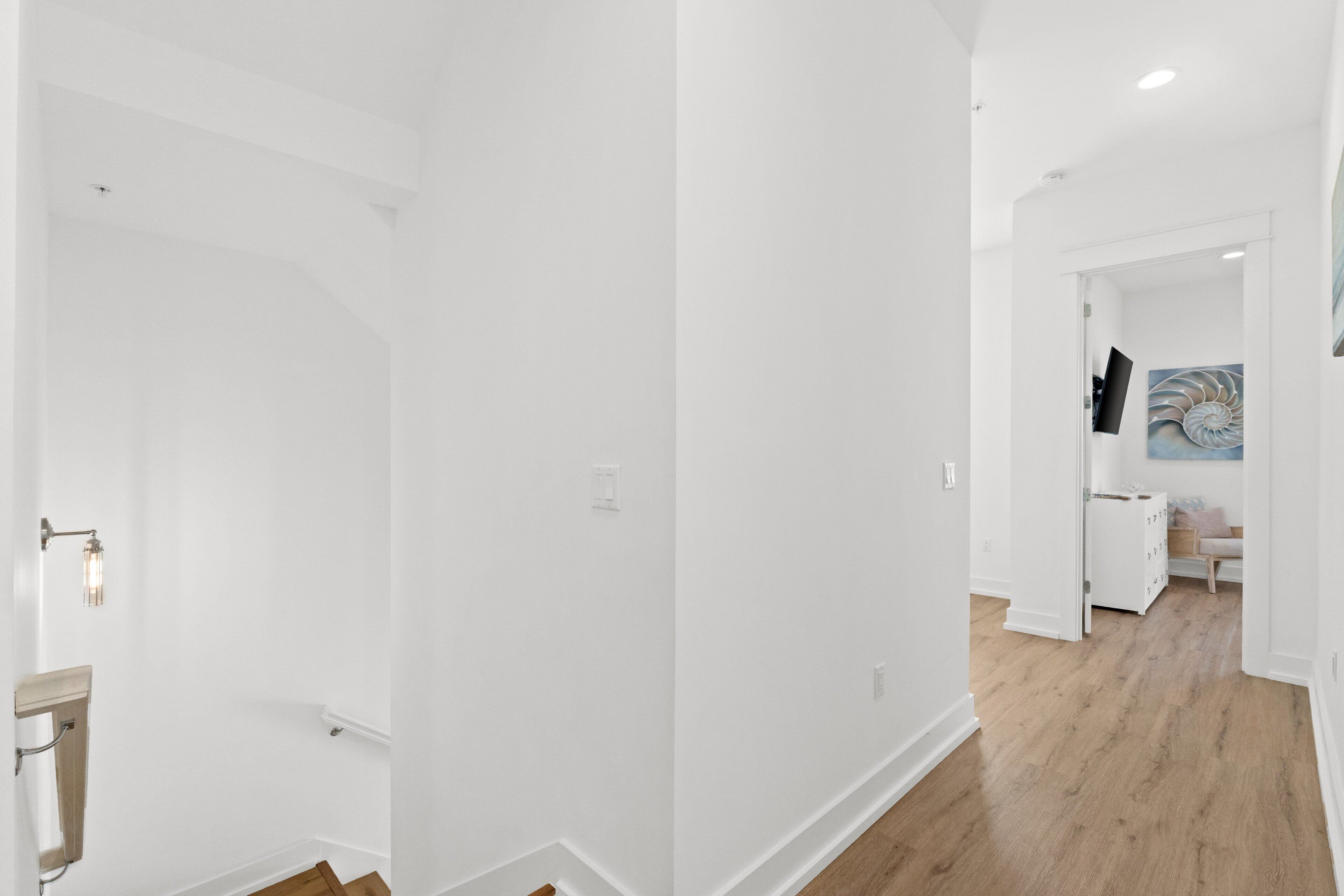Una habitació moderna amb parets blanques, sòl de fusta, una cadira integrada i un televisió de pantalla plana penjada a la paret.