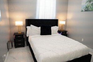 Ein ordentlich bezogenes Bett mit weißer Bettwäsche und einem schwarzen Kopfteil, flankiert von zwei Nachttischen mit Lampen, in einem Zimmer mit schlichtem, klarem Design.