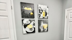 Une pièce d’angle avec une table et un banc au motif de marbre blanc, quatre œuvres d’art en noir et blanc accrochées au mur, et des portes blanches.