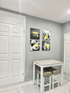 Ein Flur mit einer weißen Tür, einem kleinen weißen Tisch mit zwei Stühlen und vier schwarz-weißen Fotografien an der Wand.