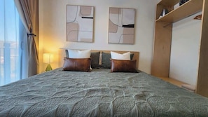 Quarto de hotel com cama, duas almofadas, luminária, arte abstrata na parede e guarda-roupa.