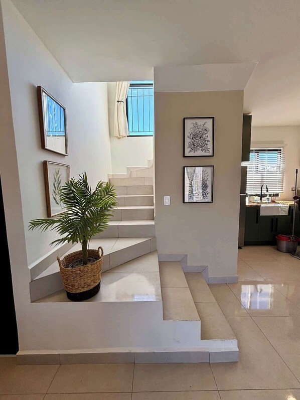 A staircase leading to a second floor, a kitchen area with a sink, and a potted plant.