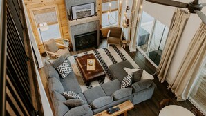 A cozy living room with a fireplace, a sofa, a coffee table, and a view of the outdoors.