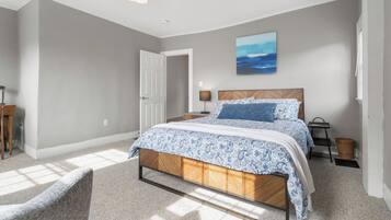 A bedroom with a bed, a nightstand, a lamp, a wall-mounted painting, and a door.