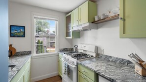 A kitchen with green cabinets, a gas stove, and a window with a view of the outside. - 1803 Historic Apartment in Heart of Salem•Steps to Haunted Happenings! (Salem)