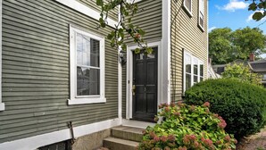 A two-story house with a front door, a window, and a brick pathway leading to the entrance. - 1803 Historic Apartment in Heart of Salem•Steps to Haunted Happenings! (Salem)