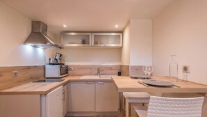A compact kitchen with a sink, stove, and cabinets. There is a dining area with a table and chairs. - Appartement Couttet - Welkeys (Chamonix-Mont-Blanc)