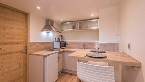 A compact kitchen with wooden cabinetry, a built-in microwave, a stainless steel range hood, and a small refrigerator. - Appartement Couttet - Welkeys (Chamonix-Mont-Blanc)