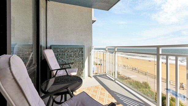 A balcony with a view of the beach, a patterned wall, and two lounge chairs.